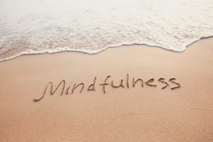 Waves lapping on the shore with the word Mindfulness written in the sand on the beach