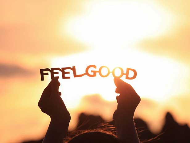 A paper cutout of the words FEEL GOOD held up against a sunset background